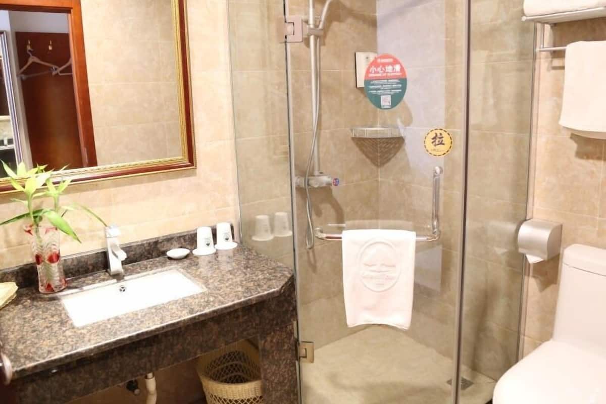 Une salle de bain dotée d’une douche à parois de verre, d’un lavabo avec un plan de toilette en marbre et d’une serviette suspendue à un porte-serviettes.