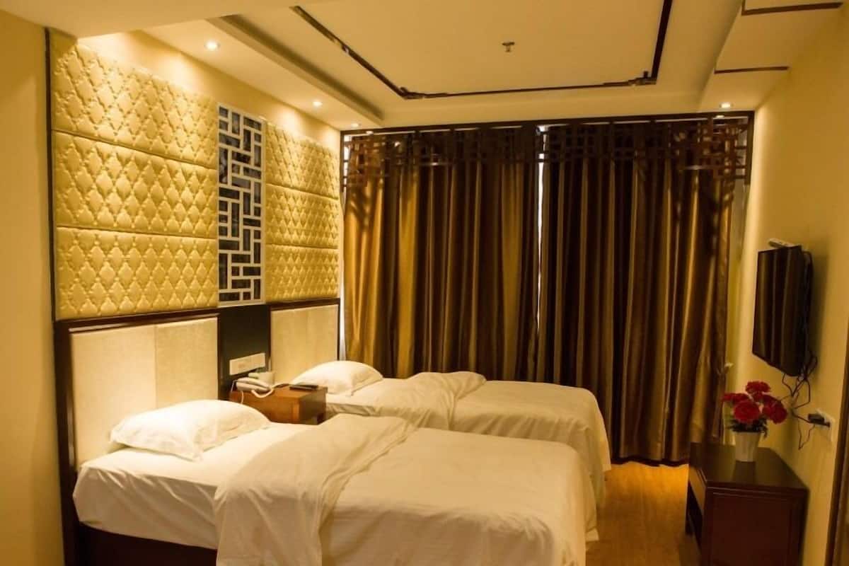 Une chambre d’hôtel avec deux lits, une grande tête de lit rembourrée, un téléviseur et une table de chevet en bois.