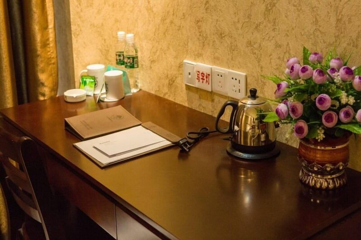 Une chambre d’hôtel avec un bureau en bois, une bouilloire, un vase avec des fleurs et des articles de toilette sur le comptoir.