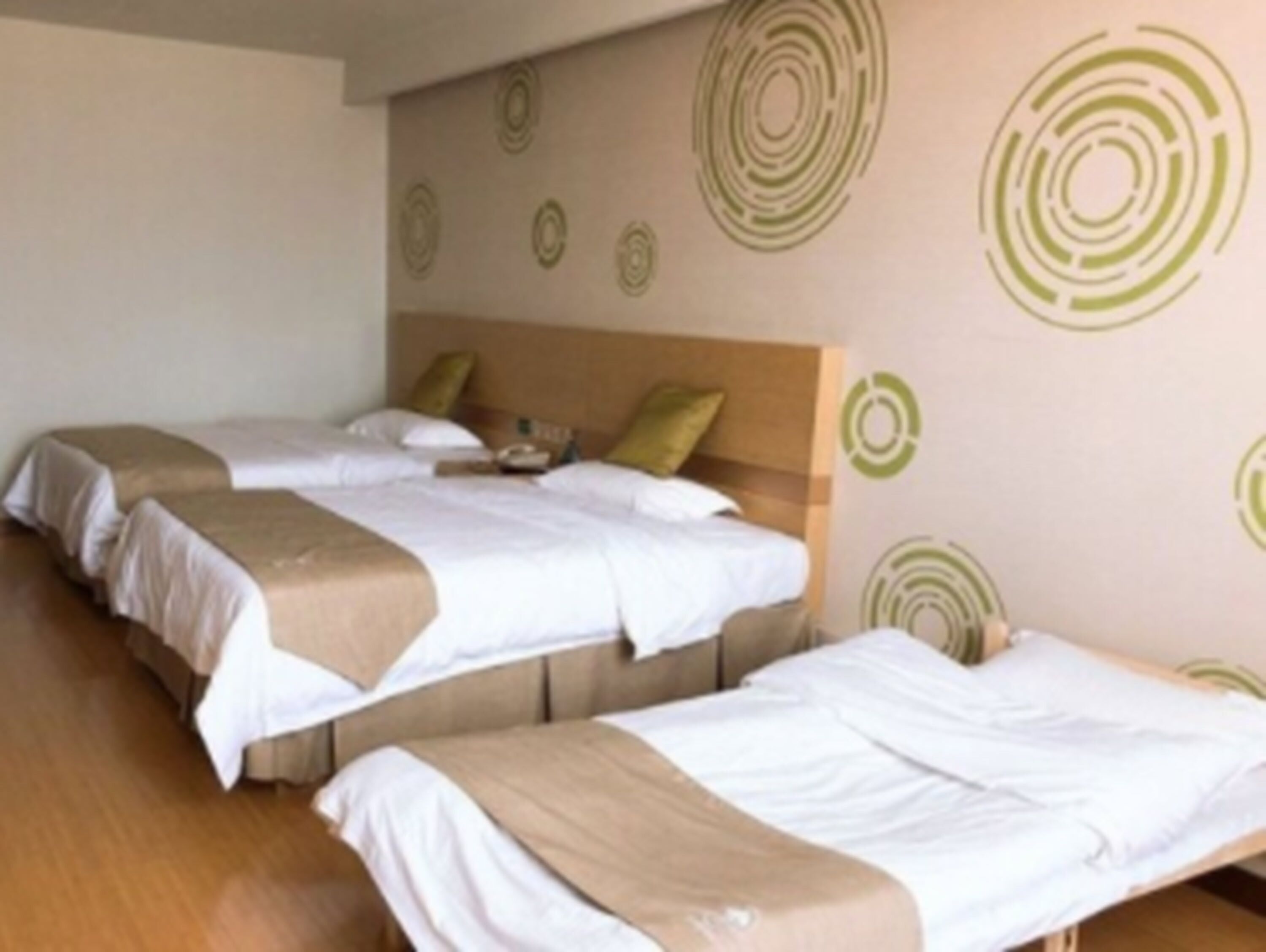 A hotel room with two single beds, a wooden headboard, and a wall with circular patterns.