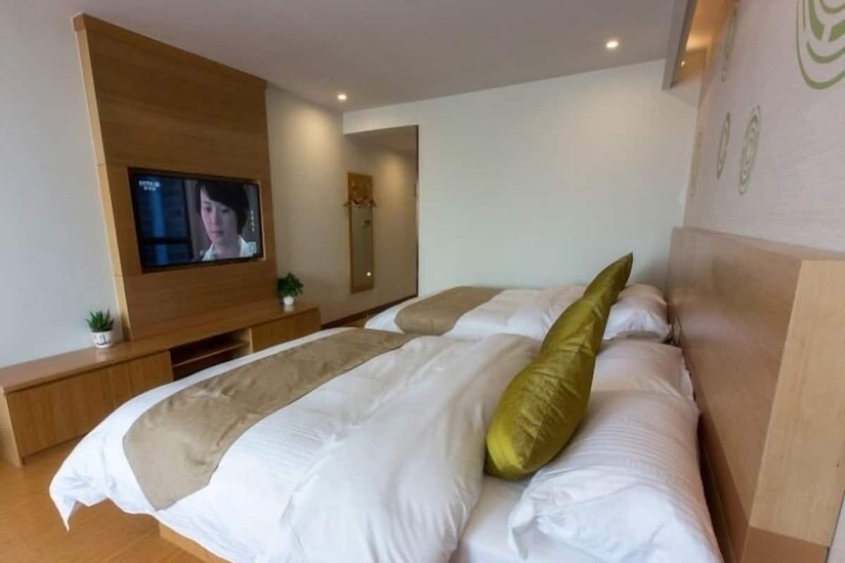 Une chambre d’hôtel moderne avec un grand lit, un téléviseur fixé au mur et une tête de lit en bois.