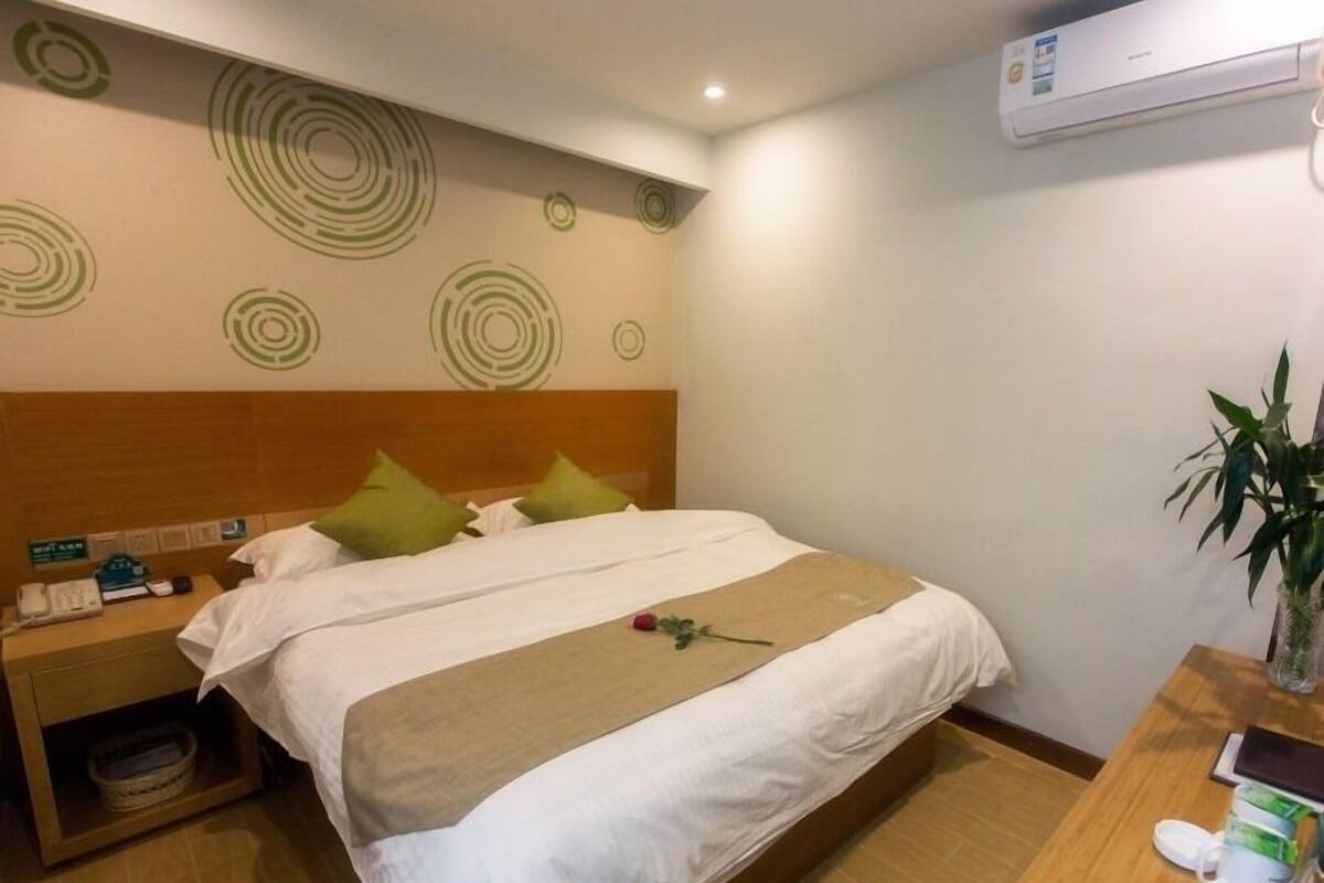 Une chambre d’hôtel comprenant un lit, une table de chevet, une petite table de nuit avec une plante et un climatiseur fixé au mur.