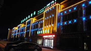 A hotel with a modern facade, illuminated signage, and a car parked in front.