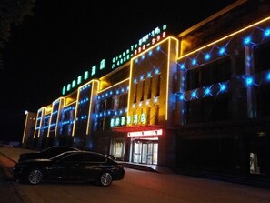 A hotel with a modern facade, illuminated signage, and a car parked in front.