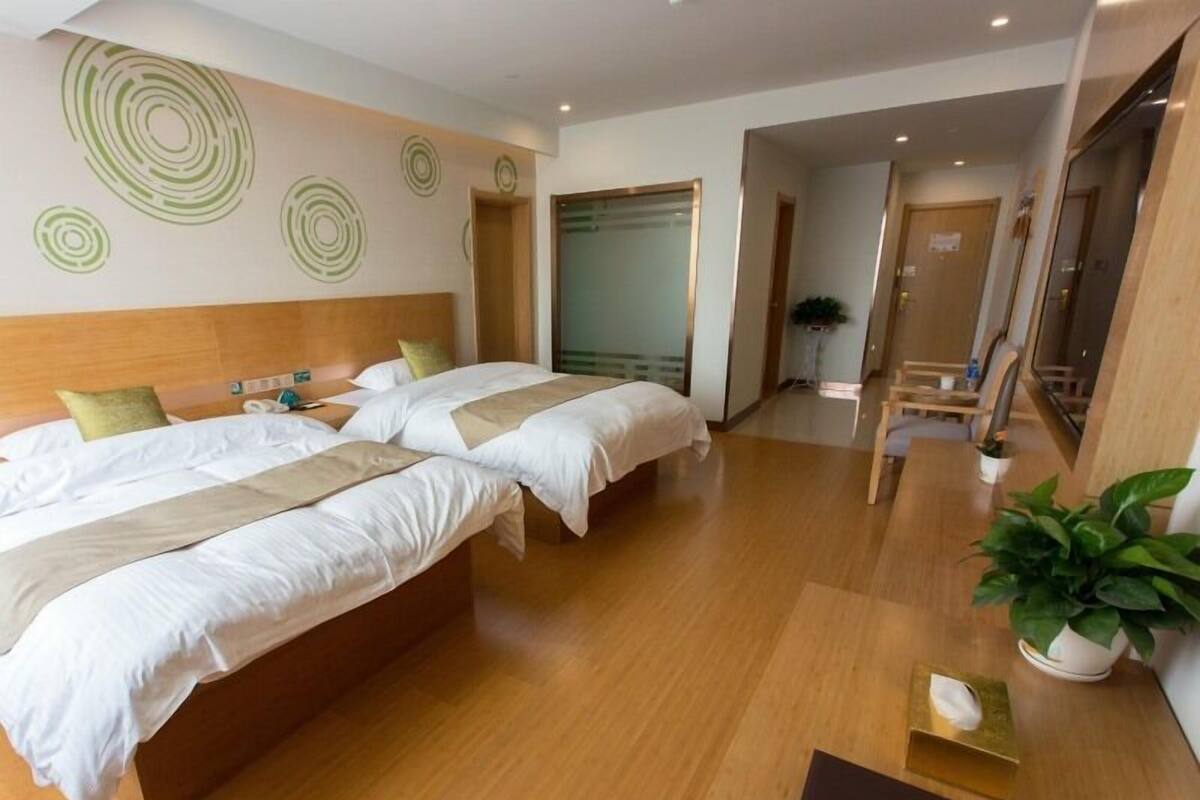Une chambre d’hôtel avec deux lits, un plancher en bois, un grand miroir et une plante en pot.
