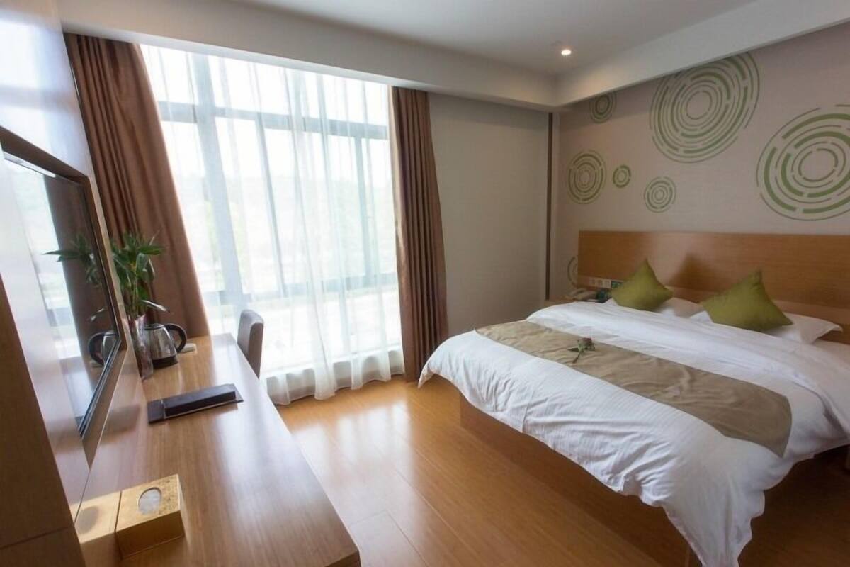 Une chambre d’hôtel avec un lit, un bureau, une chaise et une grande fenêtre avec des rideaux.