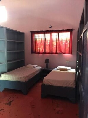 Une chambre avec deux lits simples, une petite table avec une lampe et une fenêtre avec des rideaux rouges.
