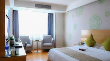 A hotel room with a bed, a desk, two chairs, a small table, and a window with curtains.