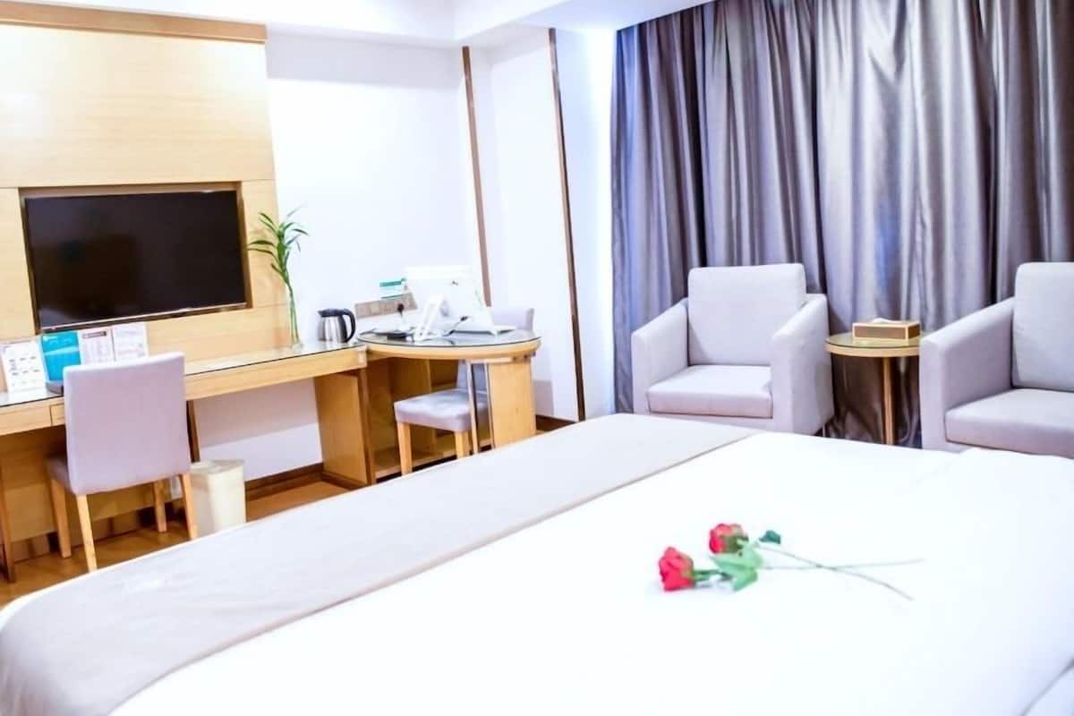 Hotelkamer met een bed, een bureau met een computer, twee stoelen, een televisie en een raam met gordijnen.