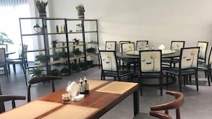 A dining area with a long wooden table, cushioned chairs, and a black metal shelving unit with plants. - GreenTree Eastern Shaoxing Keqiao Jindizizaicheng Hotel (Shaoxing)