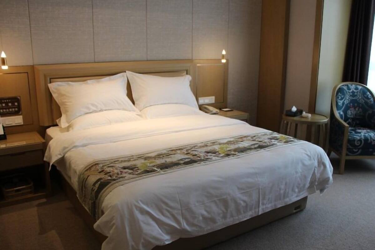 Une chambre d’hôtel avec un grand lit, une table de chevet avec une lampe, une chaise et un téléphone fixé au mur.