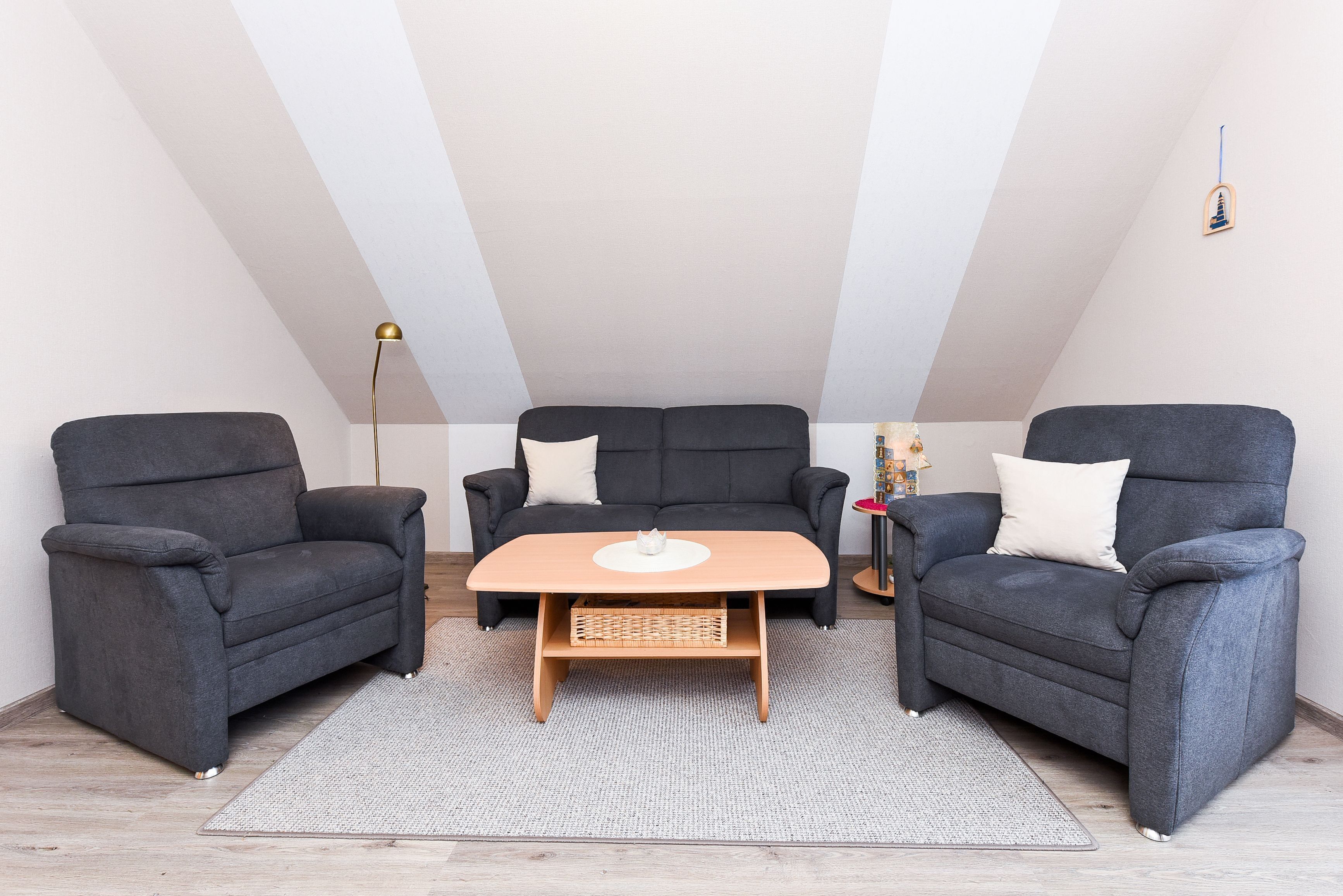 A modern loft bedroom with a high ceiling, a central sofa, two armchairs, a wooden coffee table, and a floor lamp.