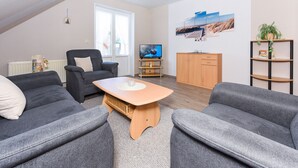 A modern living room with a sofa set, a wooden coffee table, a TV, and a bookshelf. - Vacation apartment 2 - House Wiederkehr in Bensersiel (Esens)