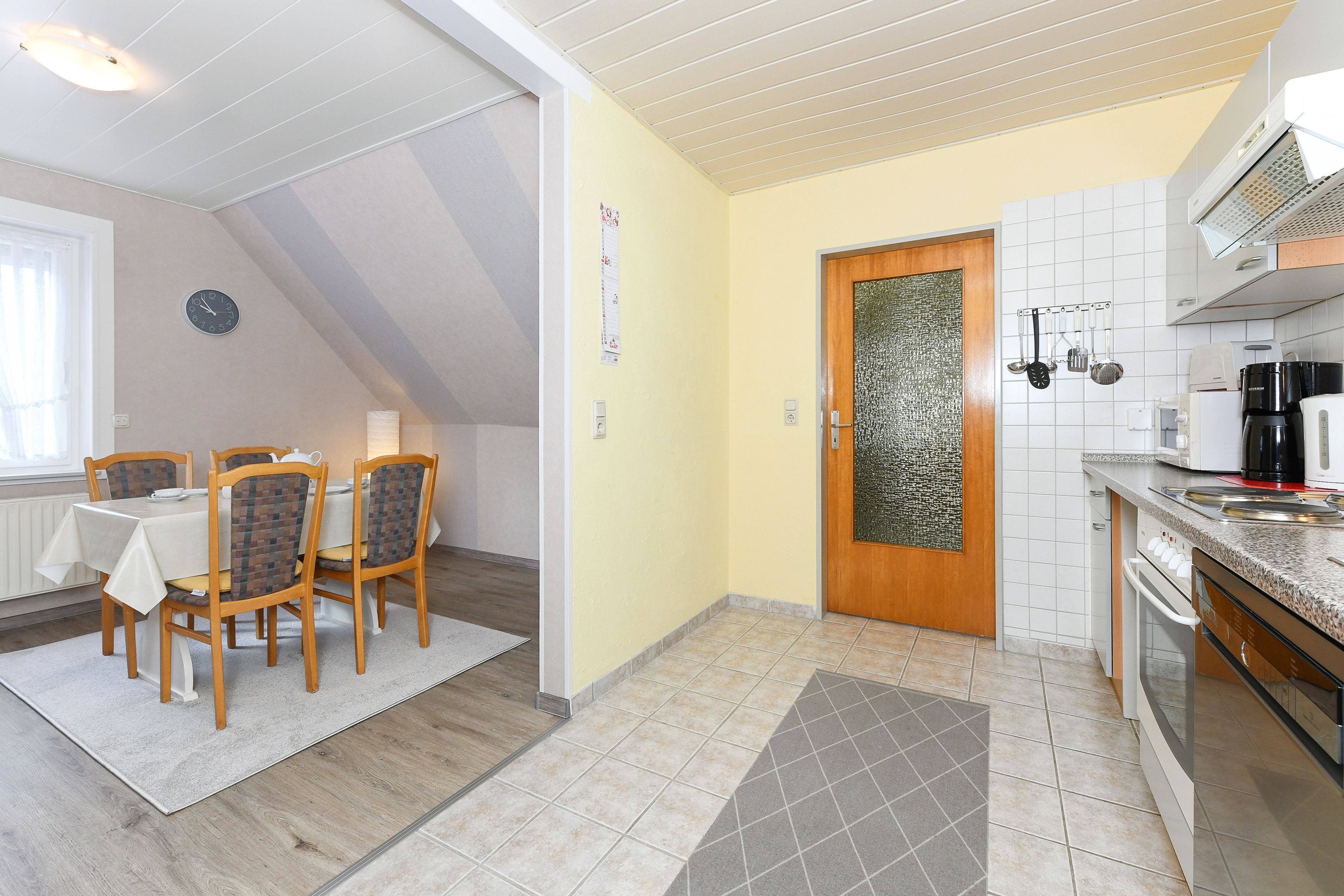 Zona pranzo con tavolo e sedie, cucina completa di elettrodomestici e una porta con pannello di vetro decorativo.