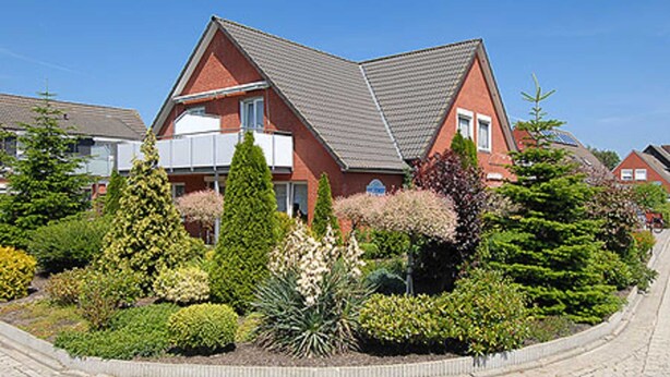 A red brick house with a grey roof, surrounded by well-maintained gardens and a cobblestone path. - Vacation apartment 2 - House Wiederkehr in Bensersiel (Esens)