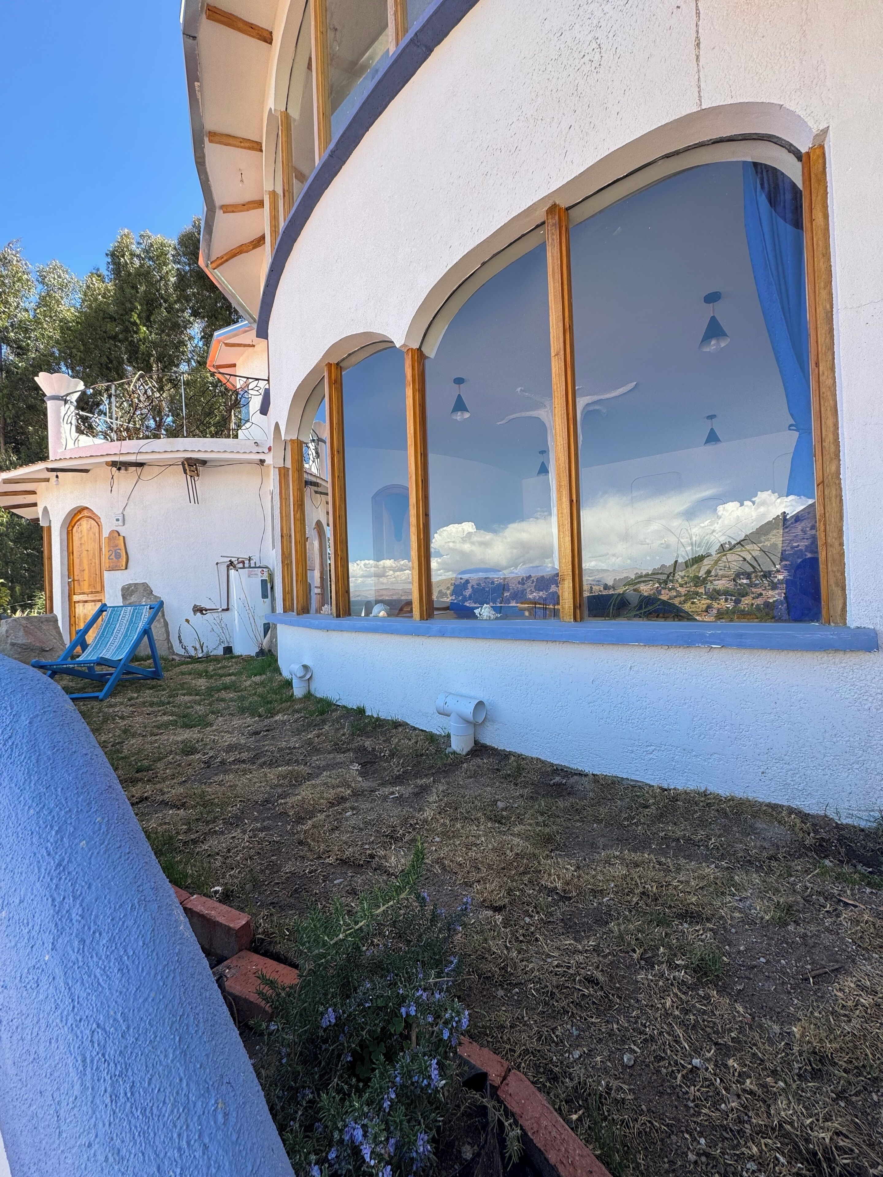 Ein Gebäude mit großen Bogenfenstern, einem blauen Stuhl davor und Blick auf eine gebirgige Landschaft.