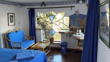 A room with a bed, a chair, a desk, a window with a view, and a trash bin.