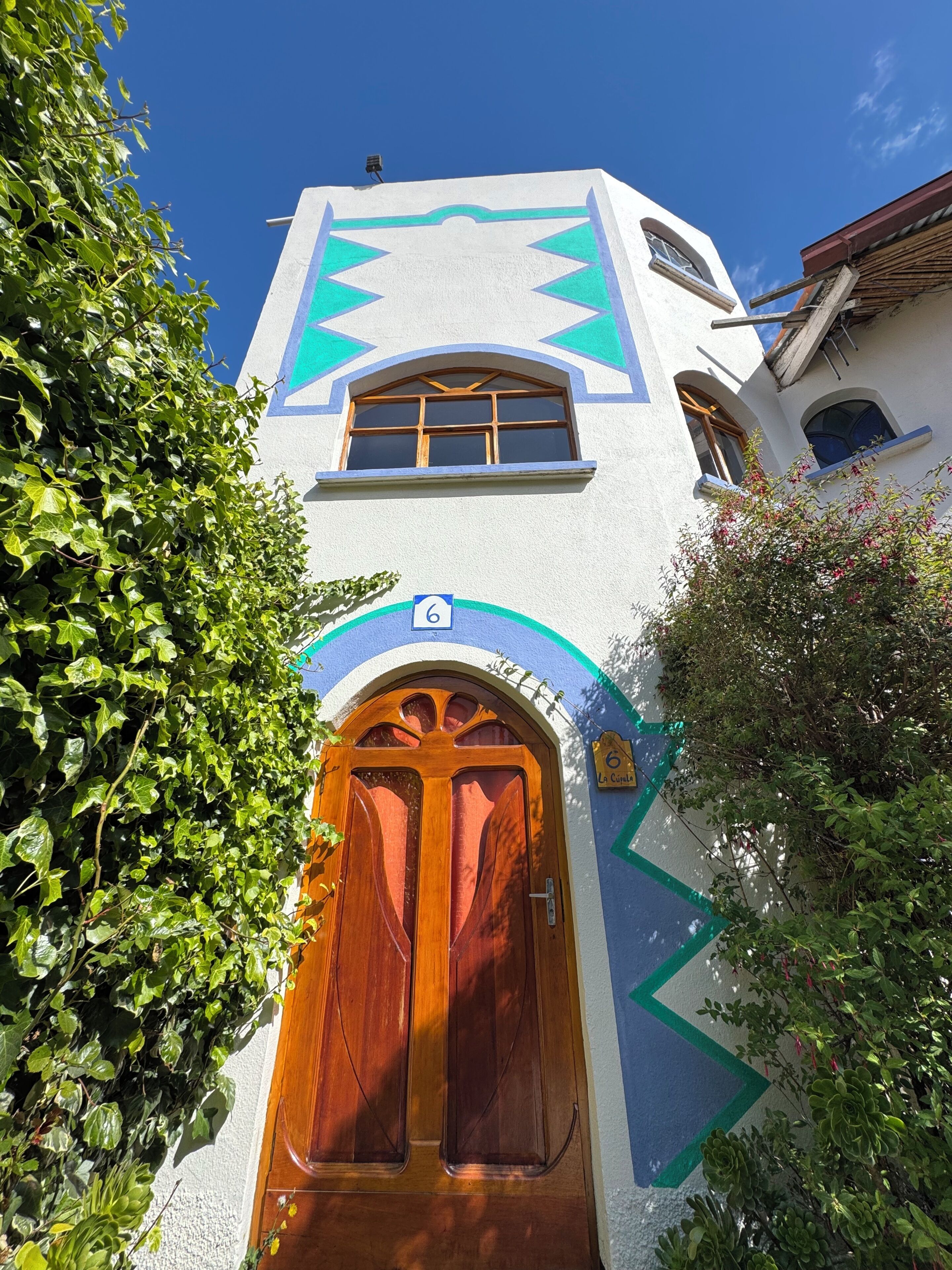 A building with a prominent arched wooden door, a window with a wooden frame, and a blue and white geometric design on the facade.