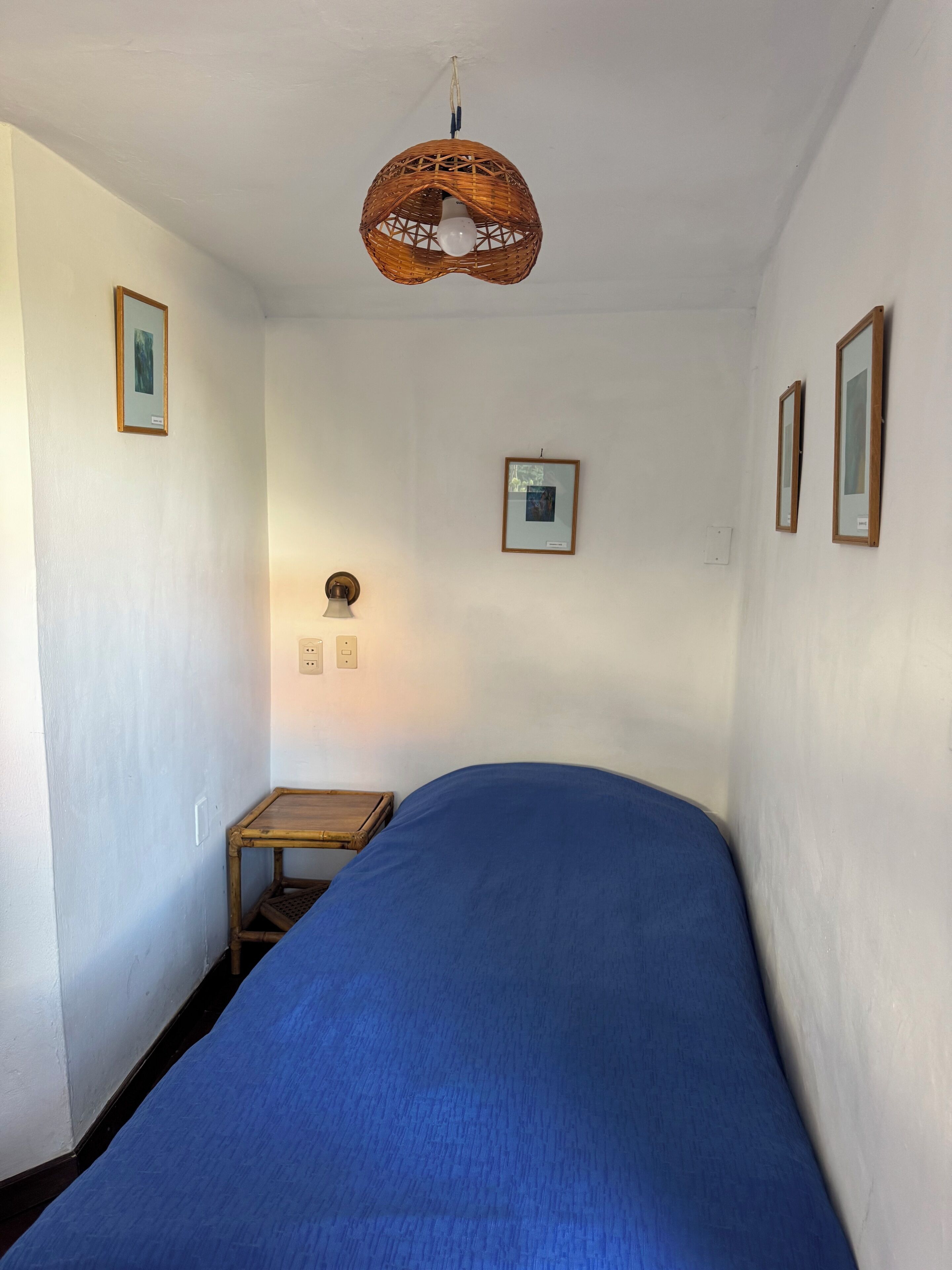 A narrow room with a single bed, a small table, and a hanging light fixture.