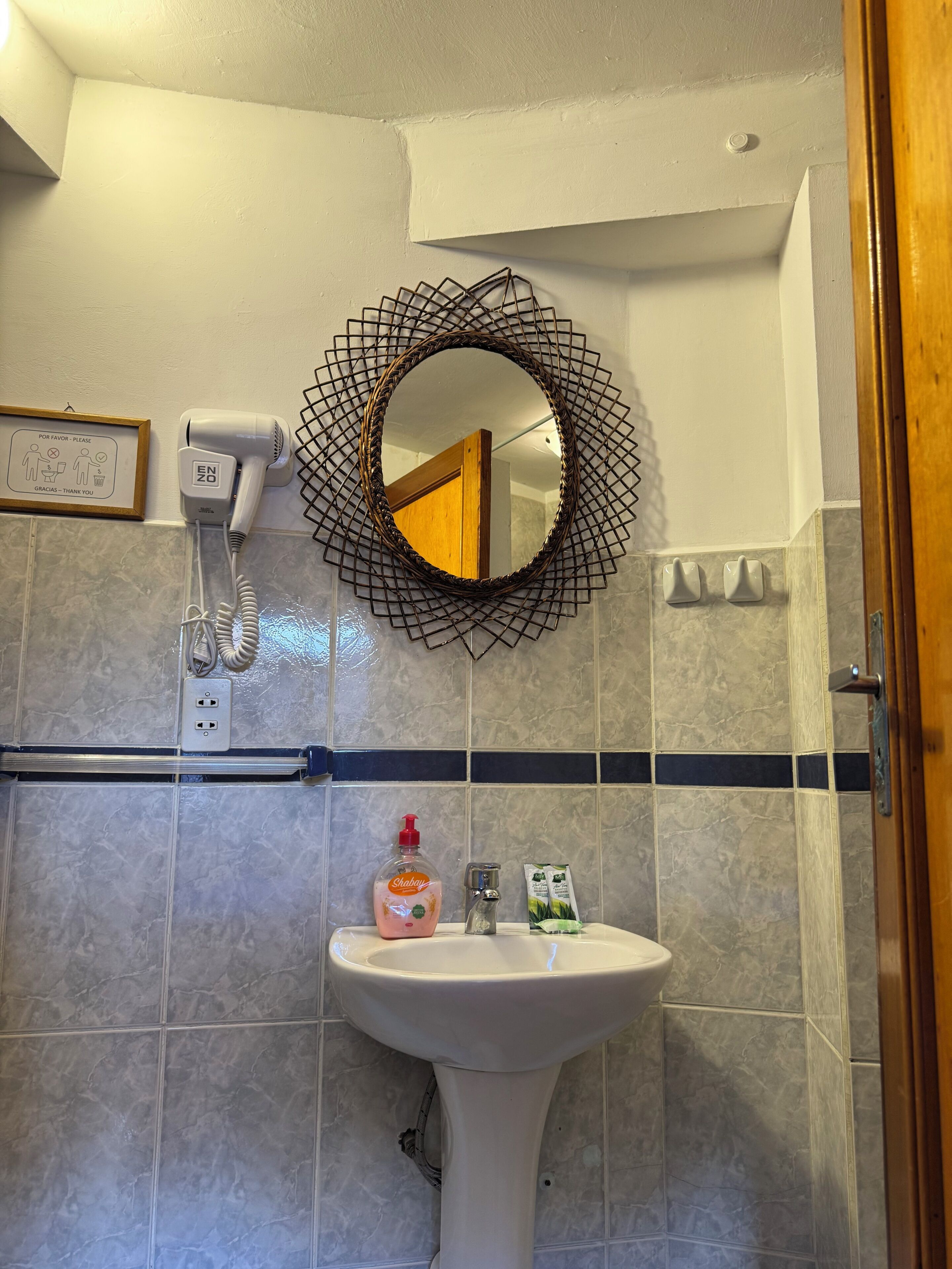 Een badkamer met een wit wastafelmeubel, een spiegel met decoratieve lijst, een haardroger en toiletartikelen.