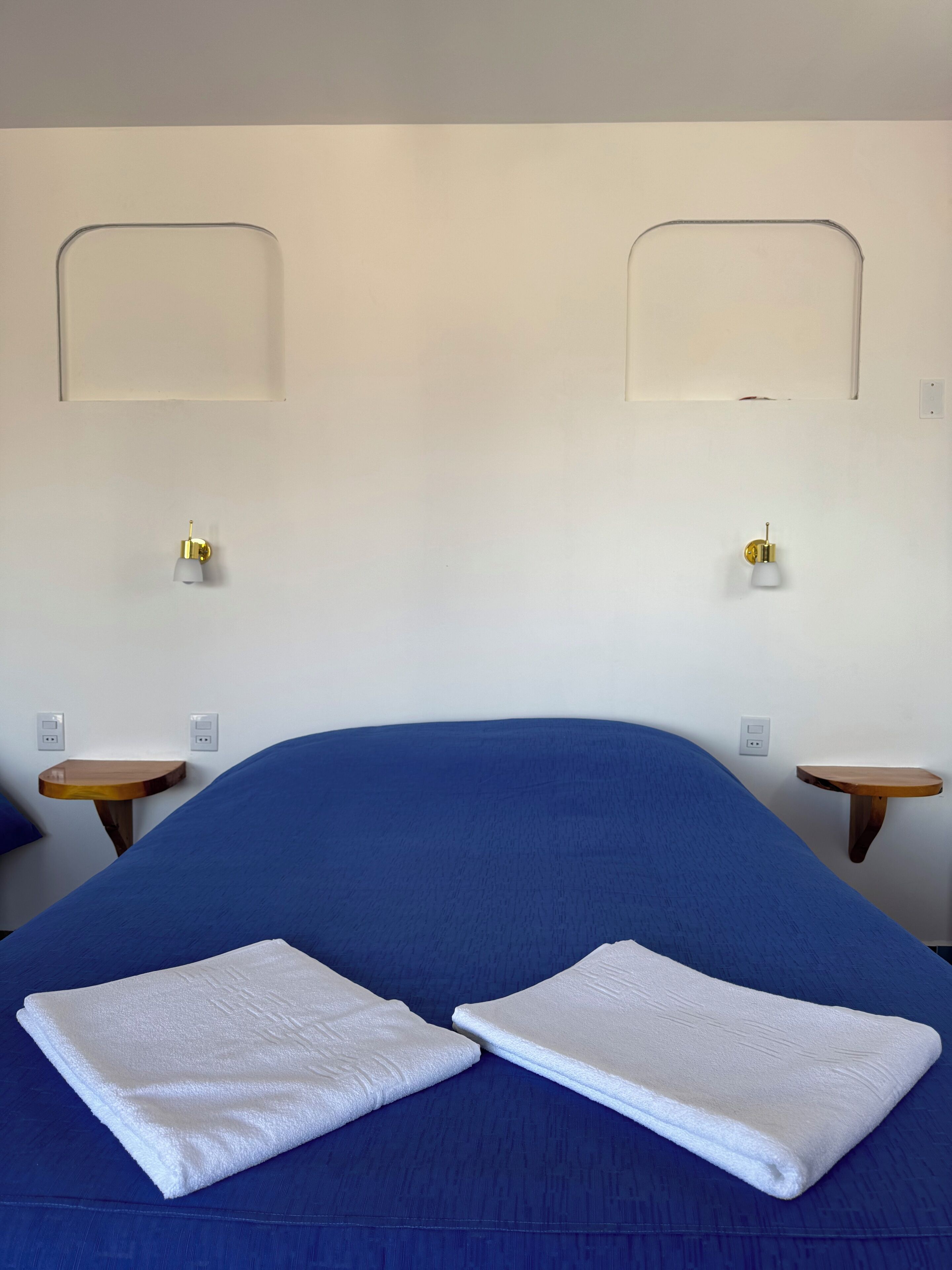 A bedroom with a large bed, two bedside tables, and wall-mounted lamps.