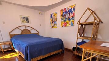 Una habitación con una cama, una mesa de madera, una silla y dos cuadros colgados en la pared.