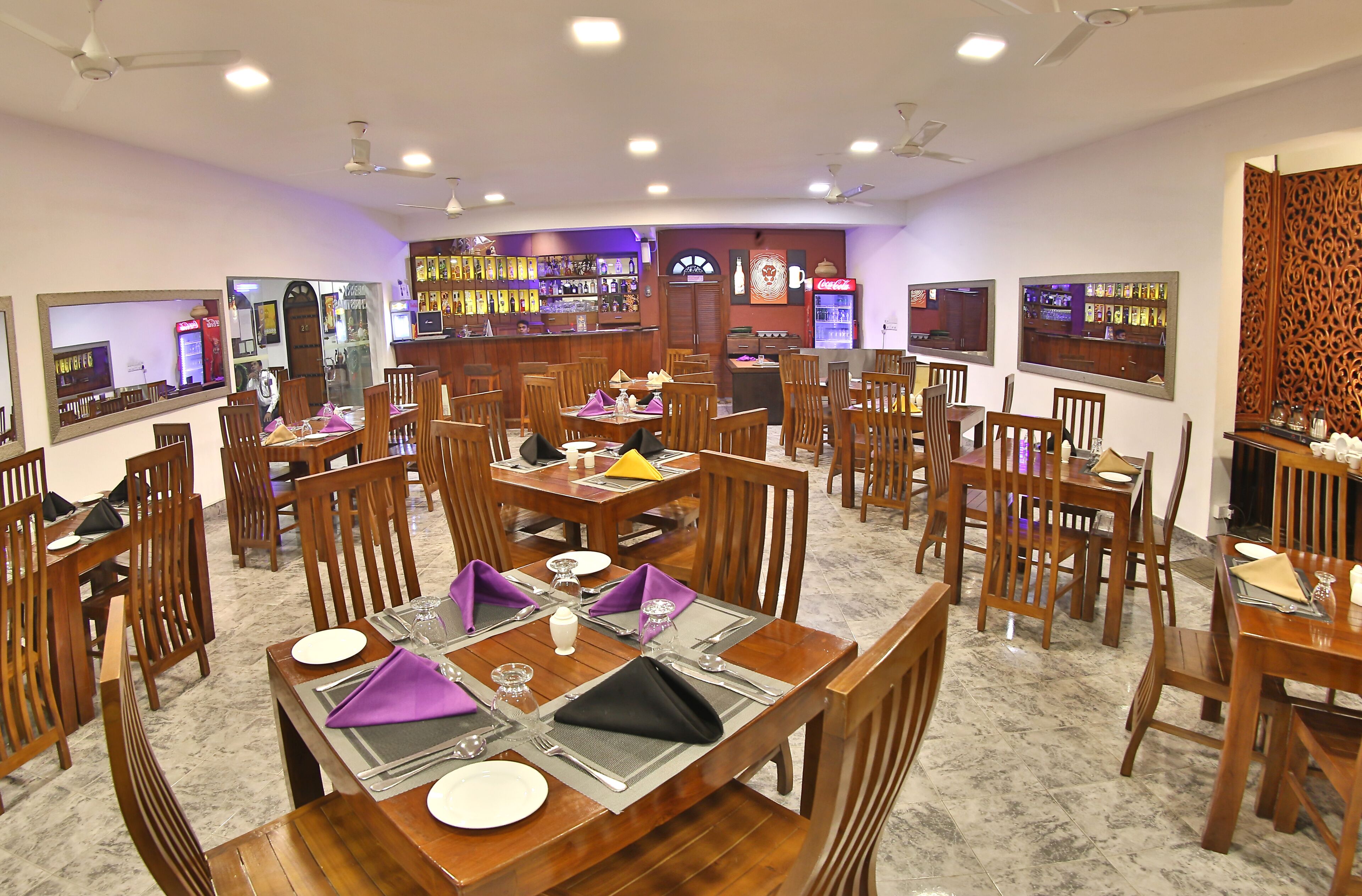A restaurant with multiple dining tables and chairs, a bar area, and a counter with a menu display.