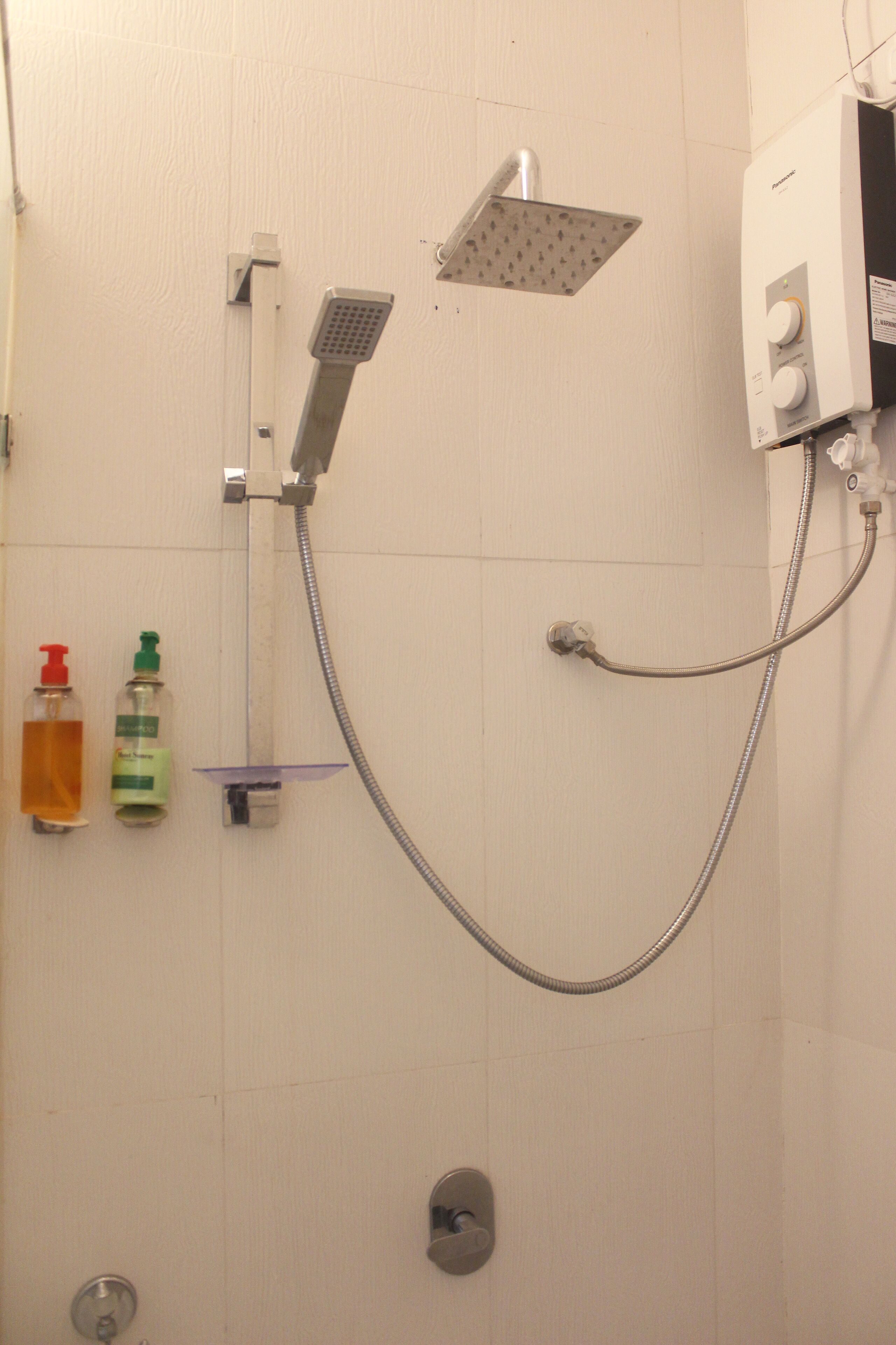 Une douche équipée d’un pommeau de douche à main et d’un pommeau de douche fixe, d’un distributeur de savon à main et d’un flacon de savon liquide.