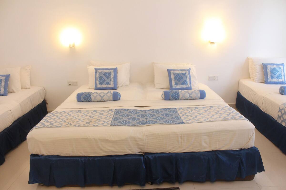 A hotel room with two single beds, each with a blue and white patterned bedspread and matching pillows. There are wall-mounted lights on either side of the bed.