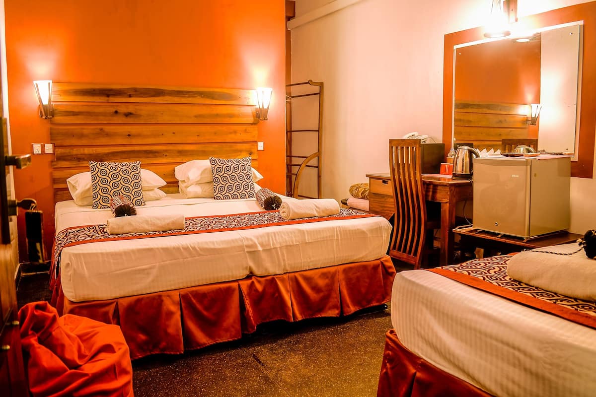 A hotel room with two beds, a wooden headboard, a mirror, a desk with a lamp, and a minibar.