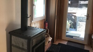 Une pièce avec un poêle à bois, une fenêtre, une porte donnant sur l’extérieur et un extincteur.