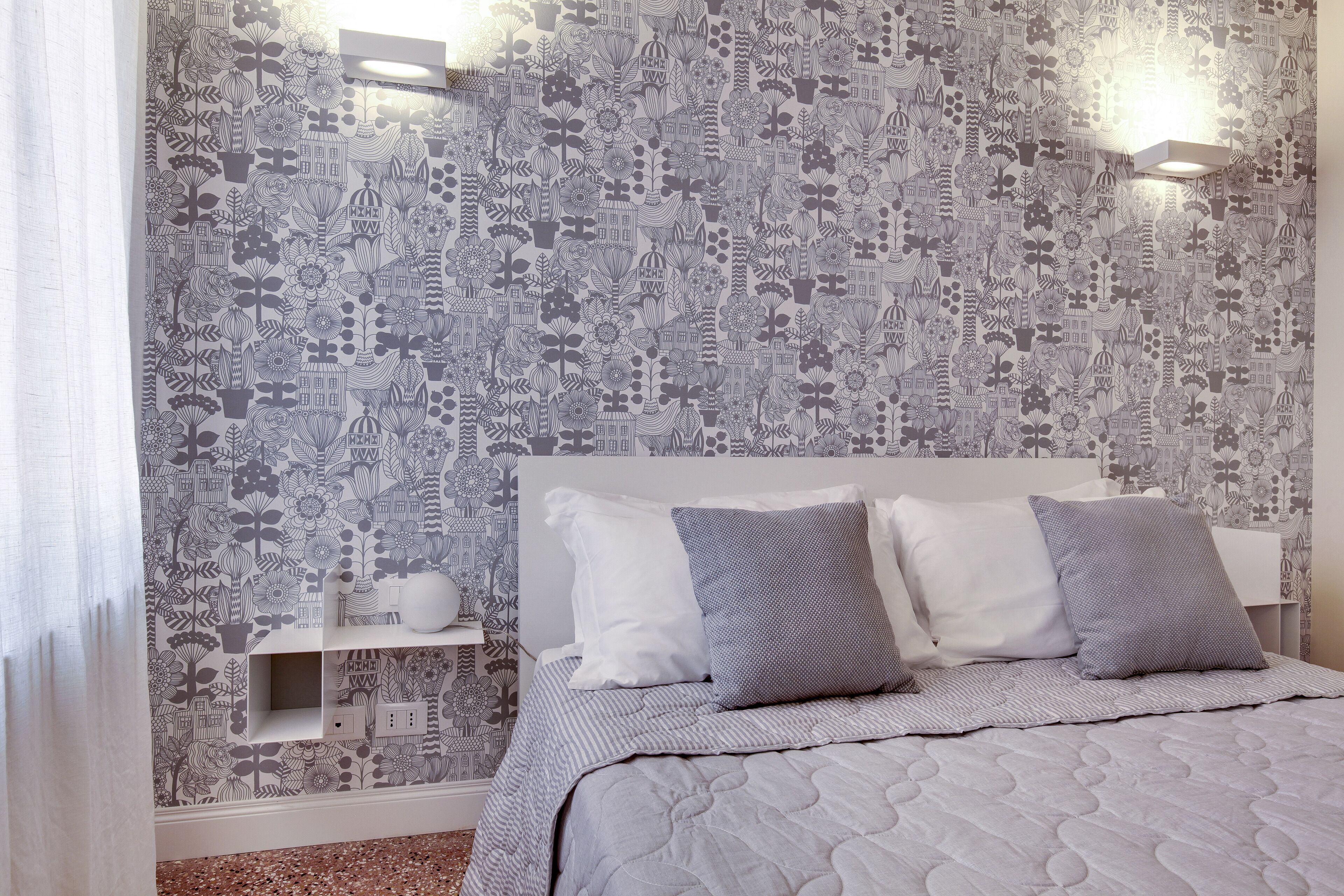 Une chambre à coucher avec un papier peint à motifs, une tête de lit blanche et deux tables de chevet avec des lampes.