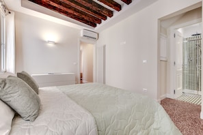A bedroom with a bed, a nightstand, a wall-mounted air conditioner, and a bathroom with a shower.