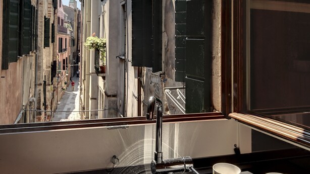 Vista d'un carrer estret des de la finestra, amb un rentaplat i dues tasses al taulell.