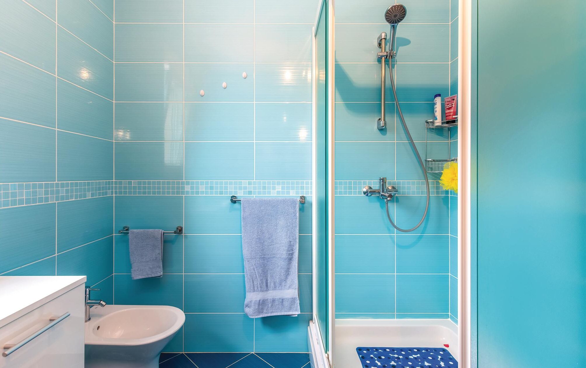 Une salle de bain avec des carreaux bleus, une douche, un bidet et une baignoire.