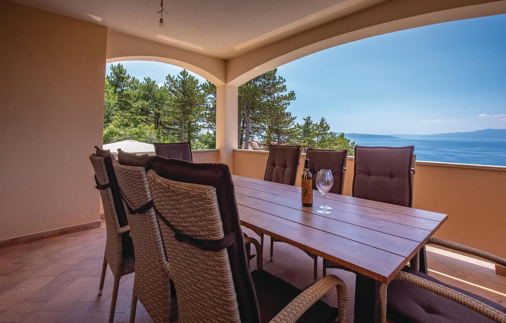 Un comedor con una mesa de madera y sillas de mimbre, con vista a un paisaje con mar y montañas.