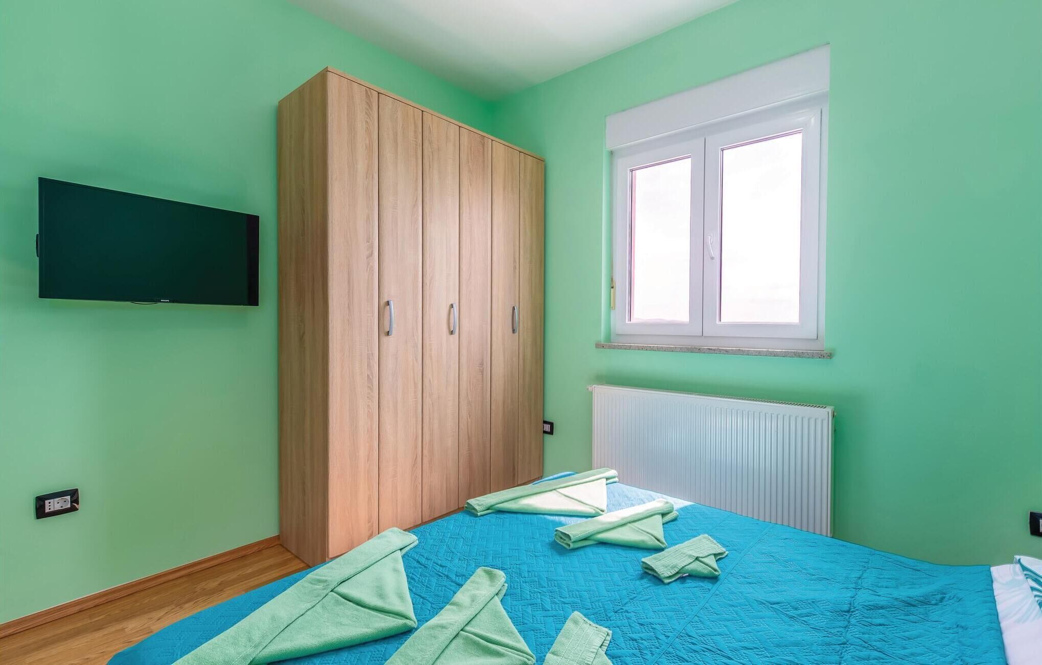 Un dormitorio con cama, armario, ventana y televisor de pared.