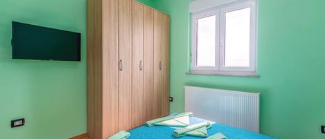 Un dormitorio con cama, armario, ventana y televisor de pared.