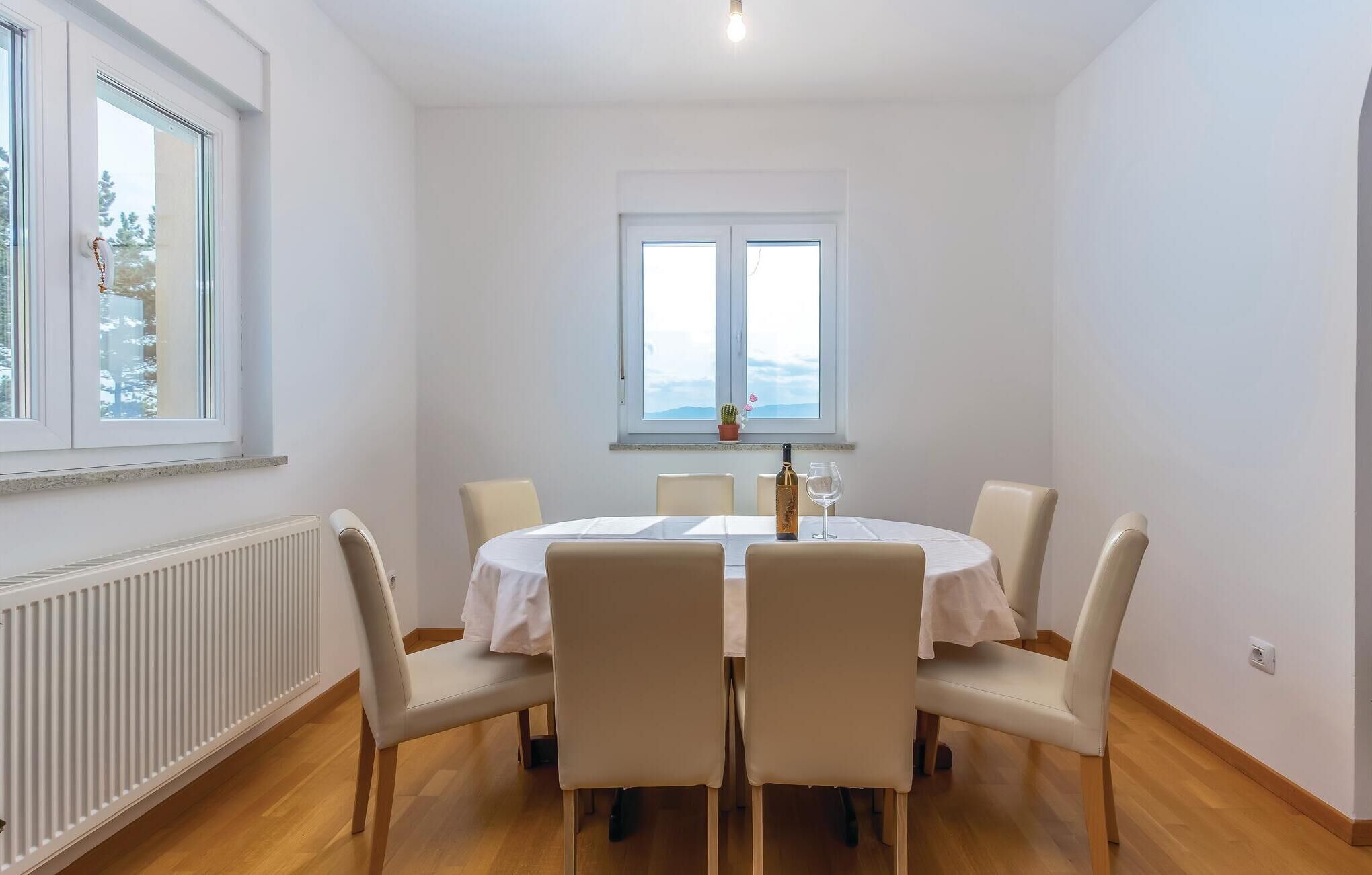 Een eethoek met een ronde tafel, vier stoelen, een fles wijn en een glas op tafel.