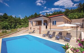 Relax by the pool surrounded by lush greenery and a stone wall.