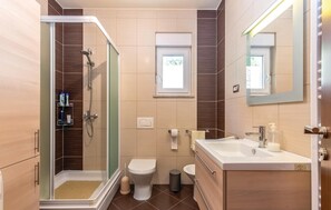 Enjoy a refreshing shower with a handheld showerhead and separate wall-mounted showerhead, plus a toilet, bidet, and sink with a soap dispenser.
