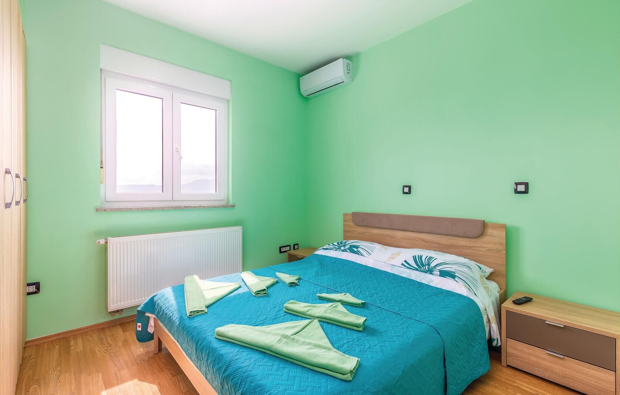 Ein Schlafzimmer mit Bett, Fenster, Klimaanlage, Nachttisch und Beistelltisch.