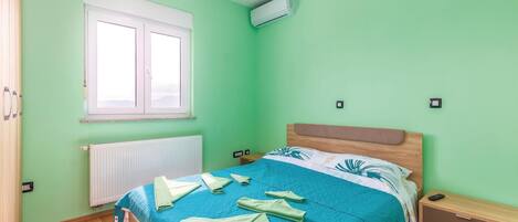 Ein Schlafzimmer mit Bett, Fenster, Klimaanlage, Nachttisch und Beistelltisch.