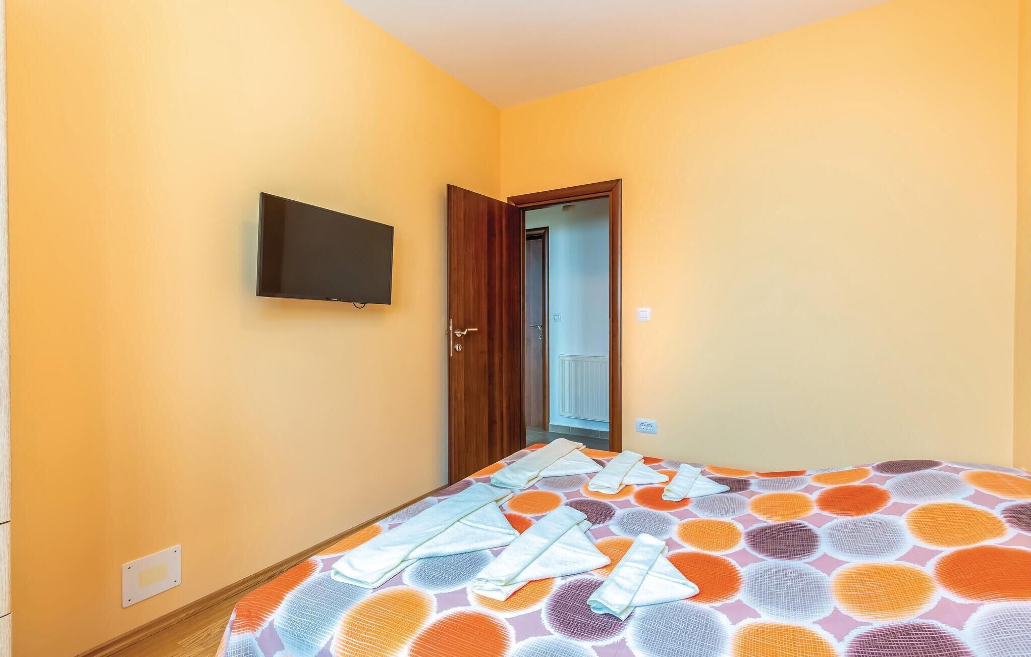 Ein Schlafzimmer mit einem Bett, einem an der Wand montierten Fernseher und einer Tür zu einem anderen Raum.