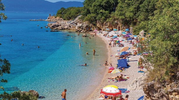 A beach with clear blue water, rocky terrain, and people sunbathing. - Beach front home in Kostrena (Kostrena)