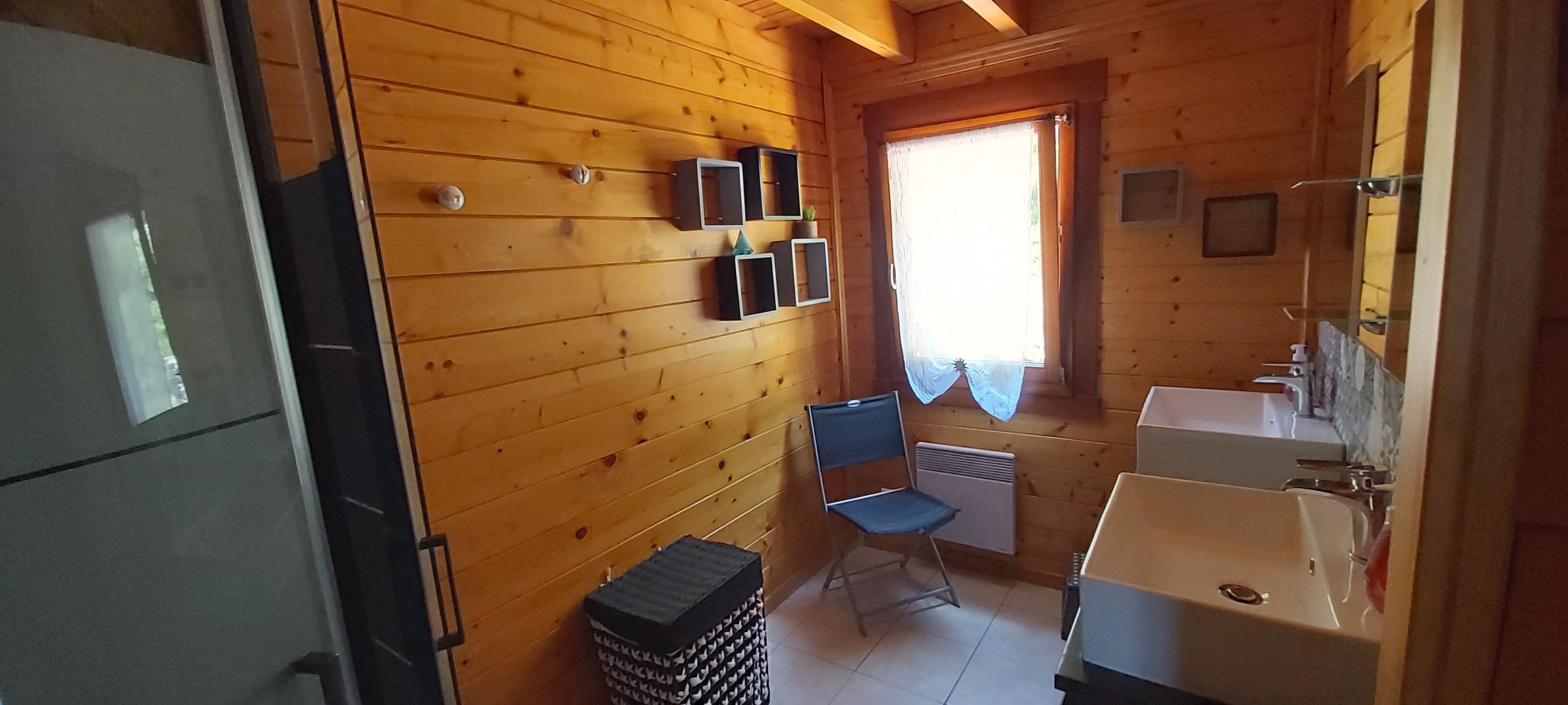 Una cabaña de madera pequeña y acogedora, con kitchenette, una silla plegable y una ventana con cortinas.