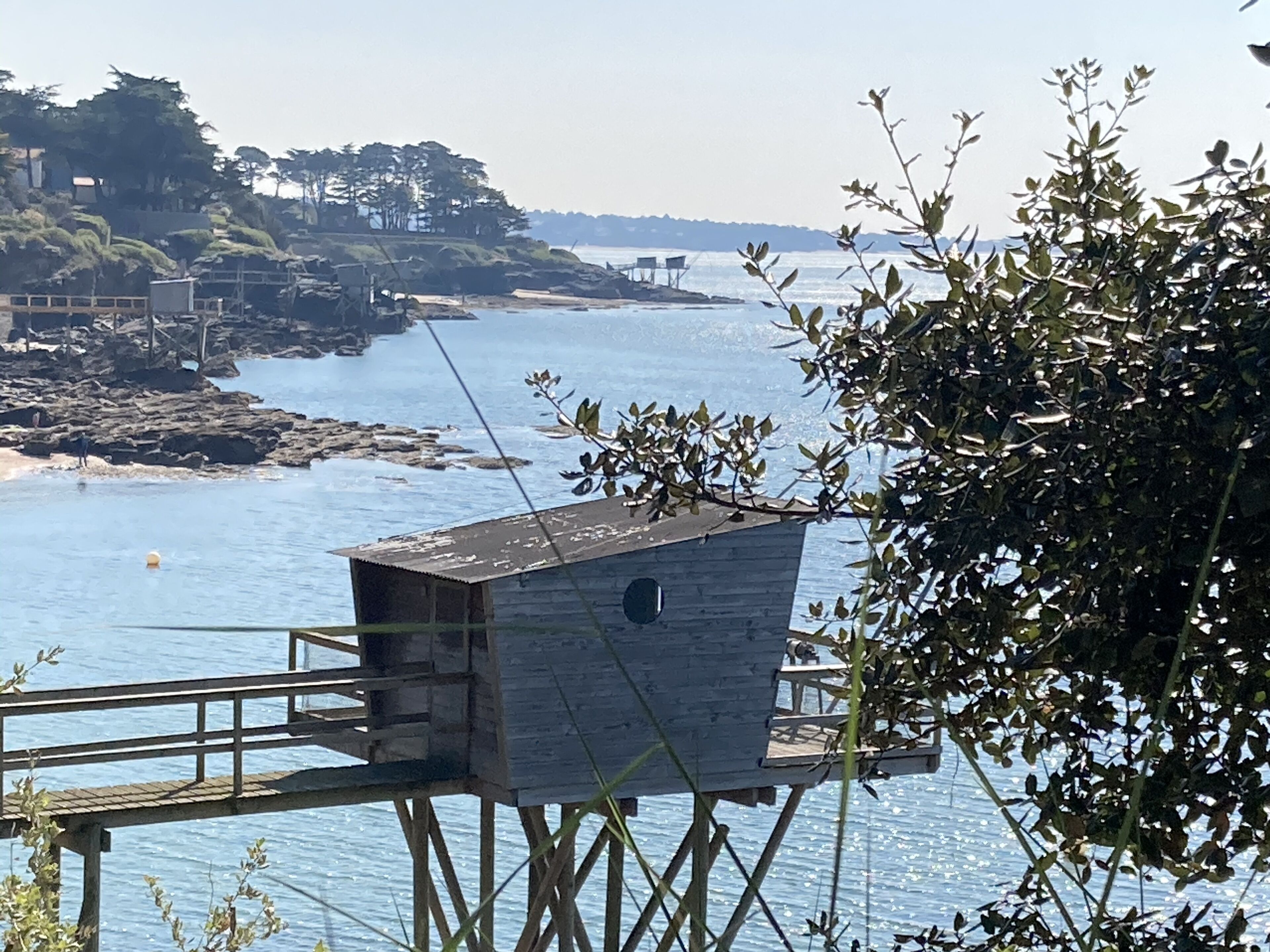 A wooden structure on stilts over water, with a view of the sea and distant land.