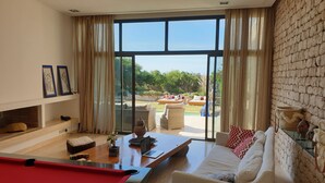 Un soggiorno con tavolo da biliardo, divano e vista su una zona esterna con piscina e poltrone relax.