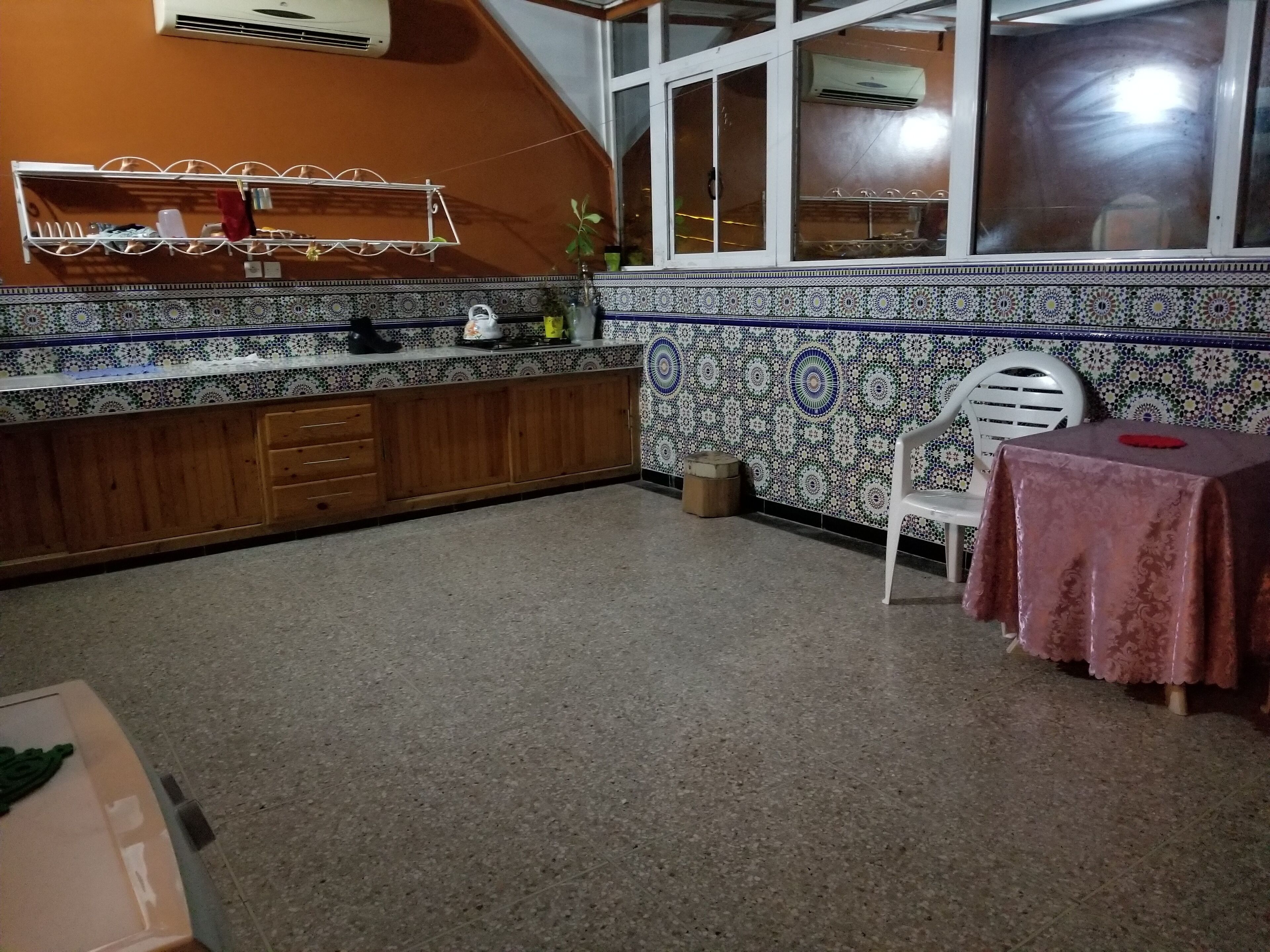 A kitchen with a tiled backsplash, wooden cabinets, a white chair, and a table with a red tablecloth.