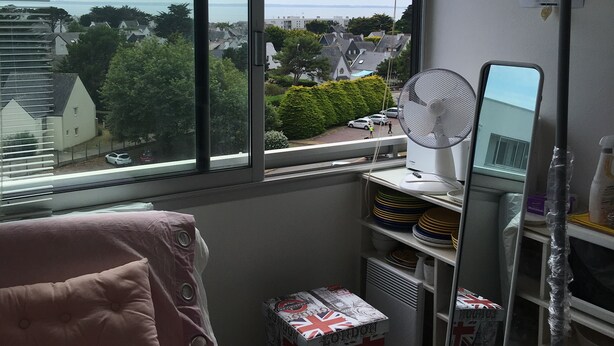 A room with a large window, a bed, a desk with a mirror, and a shelf with various items. - Sea view apartment (Quiberon)